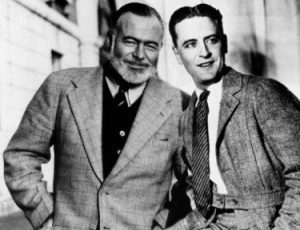 TELEVISION PROGRAMME.....OMNIBUS....F SCOTT FITZGERALD...Pictur - LeFrancophile Two men in suits stand close together, smiling and looking slightly to the right. One has a beard and checked suit; the other is clean-shaven in a lighter suit. Behind them, the blurred facade hints at Paris’s Montparnasse district.